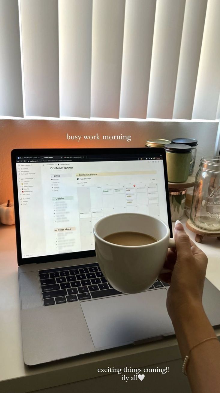 This may contain: a person holding a cup of coffee in front of a laptop