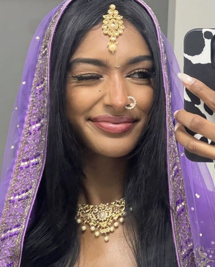This may contain: a woman wearing a purple veil and gold jewelry is taking a selfie with her cell phone