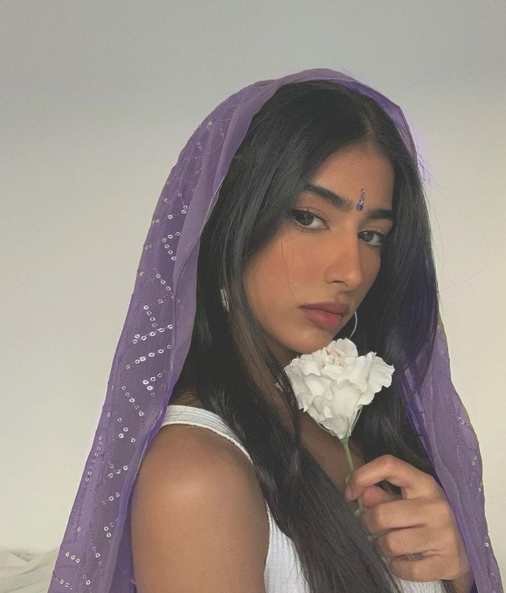 This may contain: a woman wearing a purple veil and holding a white flower