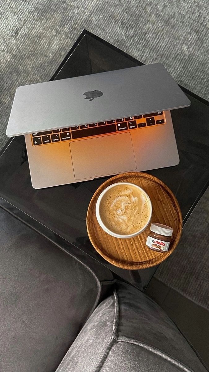 This may contain: a cup of coffee sitting on top of a wooden plate next to a laptop computer