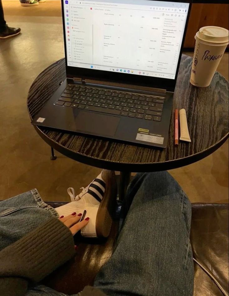 This may contain: a laptop computer sitting on top of a wooden table next to a person's legs