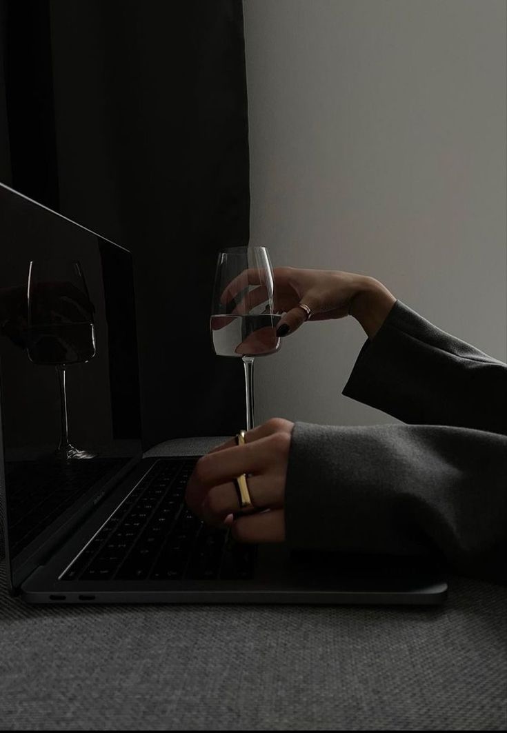 This may contain: a person holding a wine glass in front of a laptop