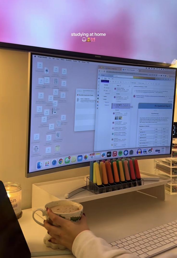 This may contain: a person sitting at a desk in front of a computer monitor holding a coffee cup