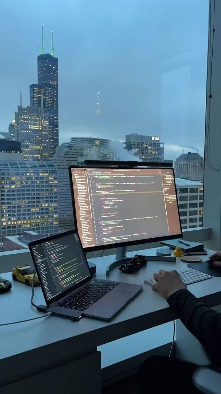 This may contain: a person sitting at a desk with two laptops and a computer monitor in front of them