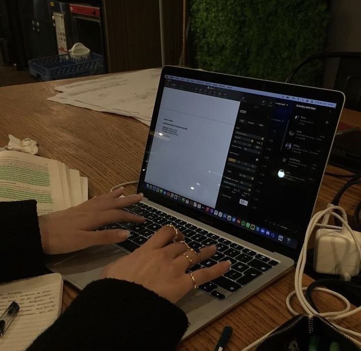 This may contain: a person using a laptop computer on a wooden table with papers and other electronic equipment