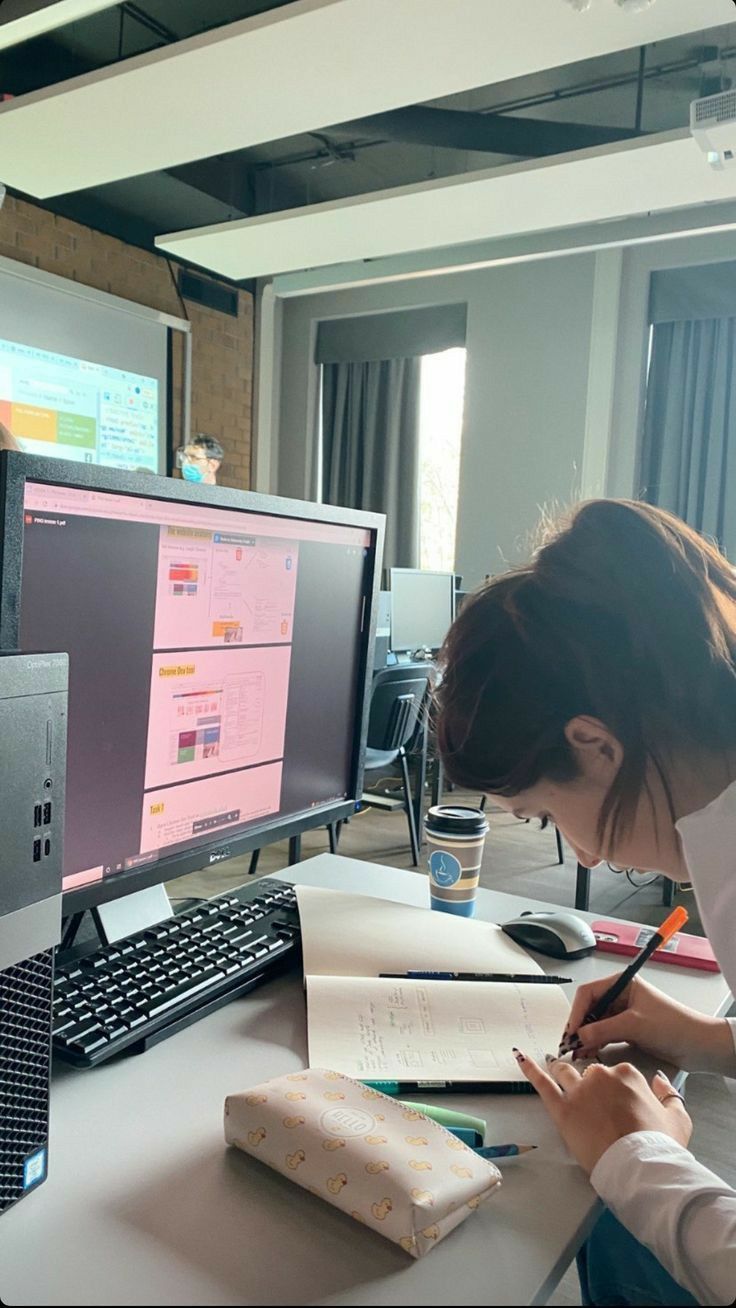 This may contain: a person writing on a piece of paper in front of a computer monitor and keyboard