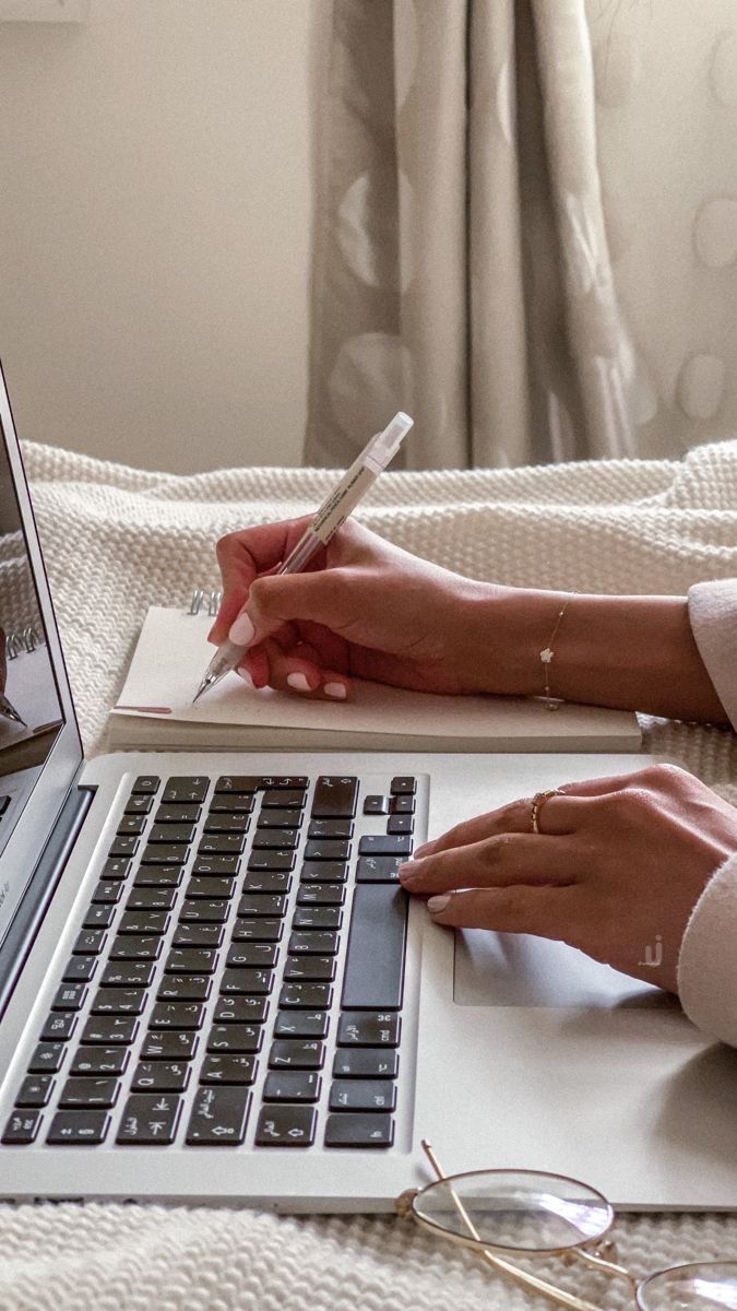 This may contain: a woman is writing on her notebook while sitting in front of an open laptop computer