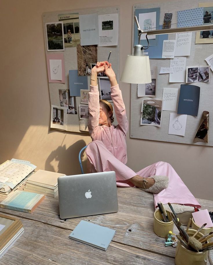 This may contain: a woman sitting at a desk with her laptop and headphones up in the air