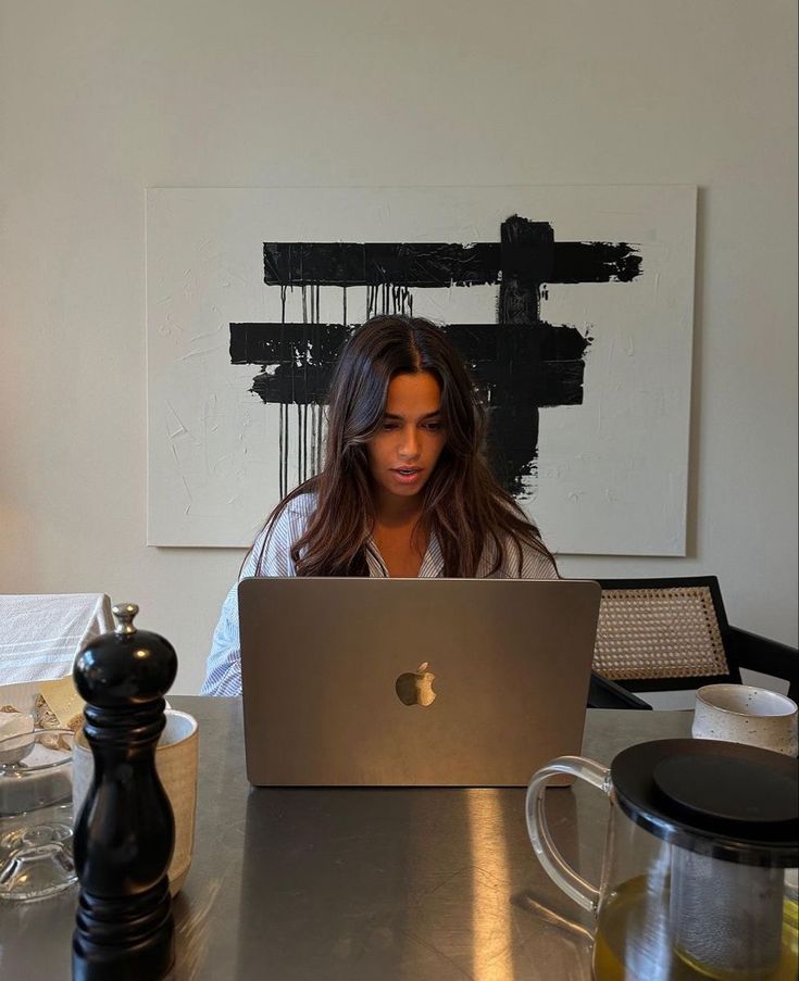 This may contain: a woman sitting at a table with a laptop computer in front of her on the desk