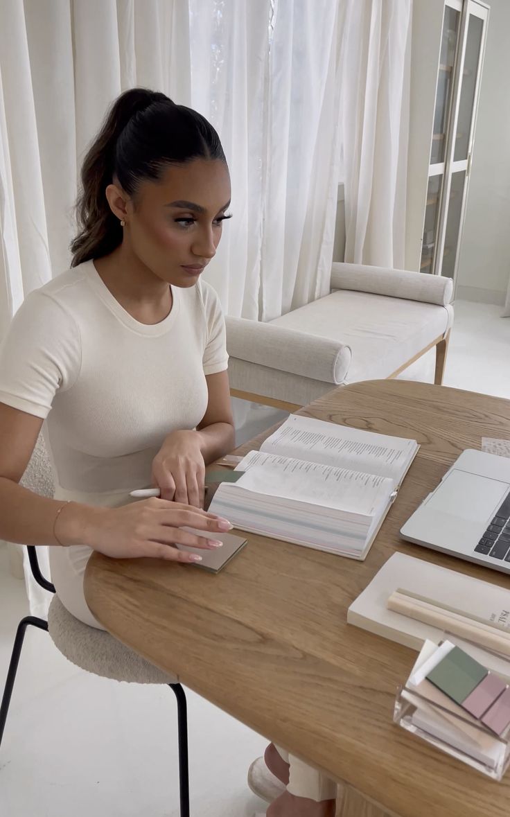 This may contain: a woman sitting at a table with an open book