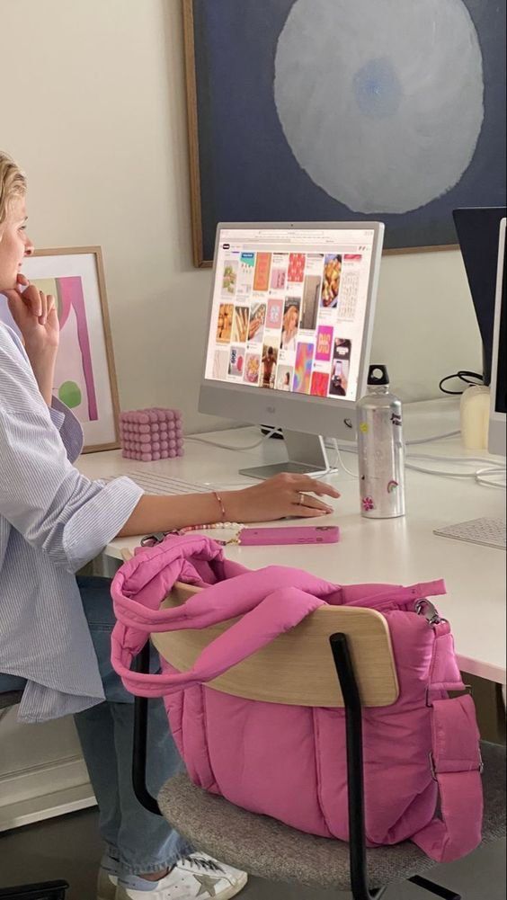This may contain: a woman sitting in front of a computer desk with a pink purse on her lap