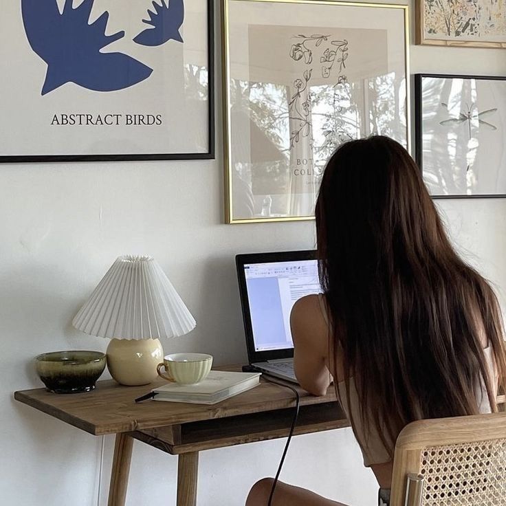 This may contain: a woman sitting in front of a laptop computer on top of a desk next to a lamp