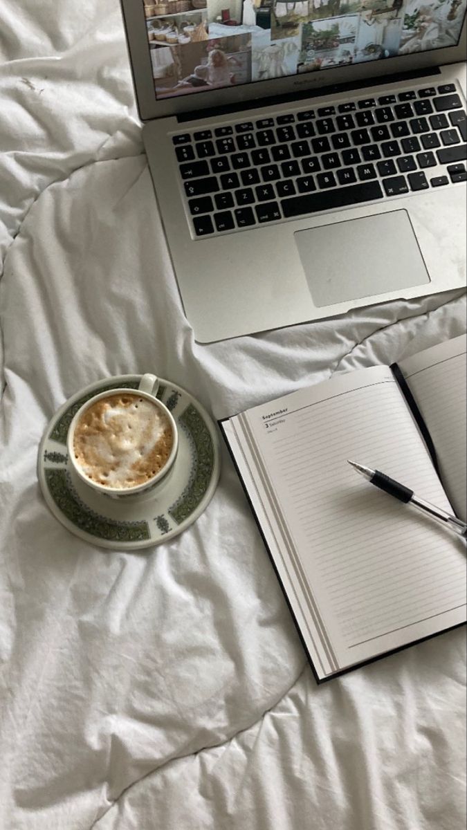 This may contain: an open laptop computer sitting on top of a bed next to a cup of coffee