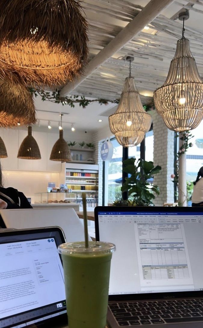 This may contain: two laptops and a drink on a table in front of some hanging light fixtures