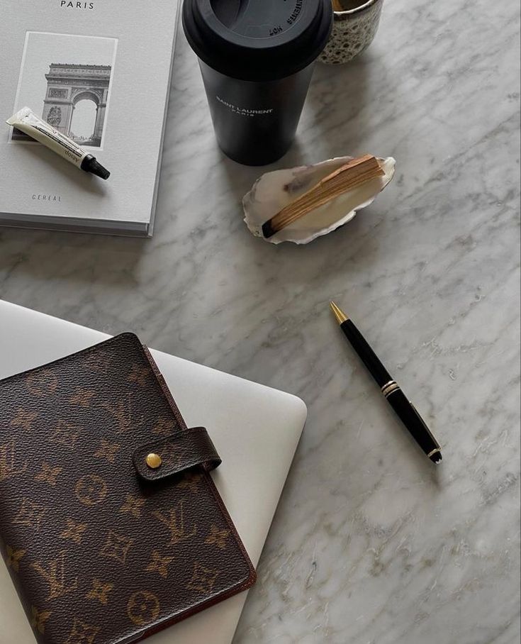 This may contain: a desk with a notebook, pen and cup on it next to a coffee mug