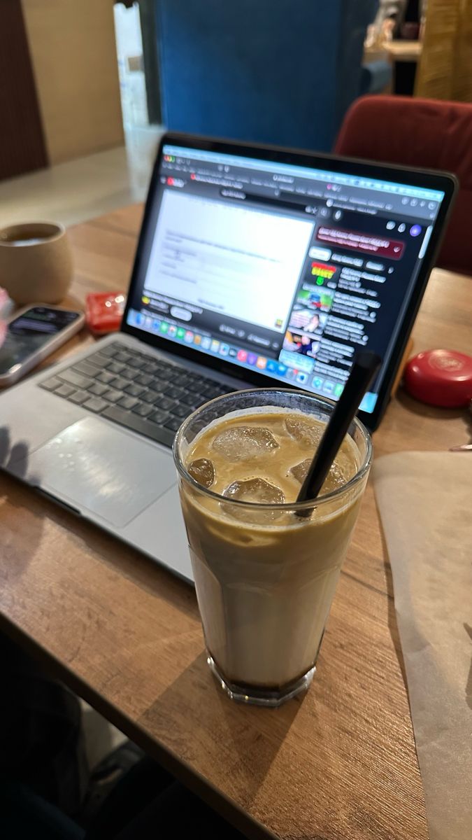 This may contain: a laptop computer sitting on top of a wooden table next to a cup of coffee