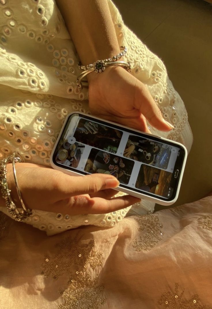 This may contain: a woman in a white dress holding a cell phone with pictures on it's screen