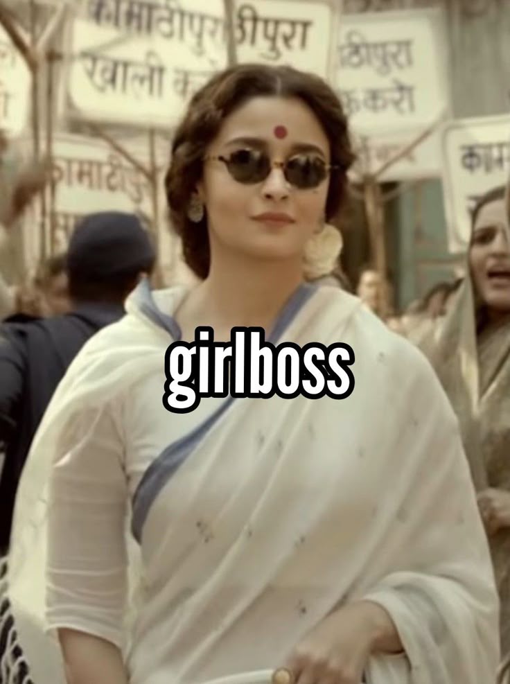 This may contain: a woman in white sari and sunglasses walking down the street with people behind her