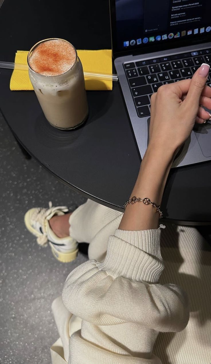 This may contain: a woman sitting at a table with a laptop computer and coffee in front of her