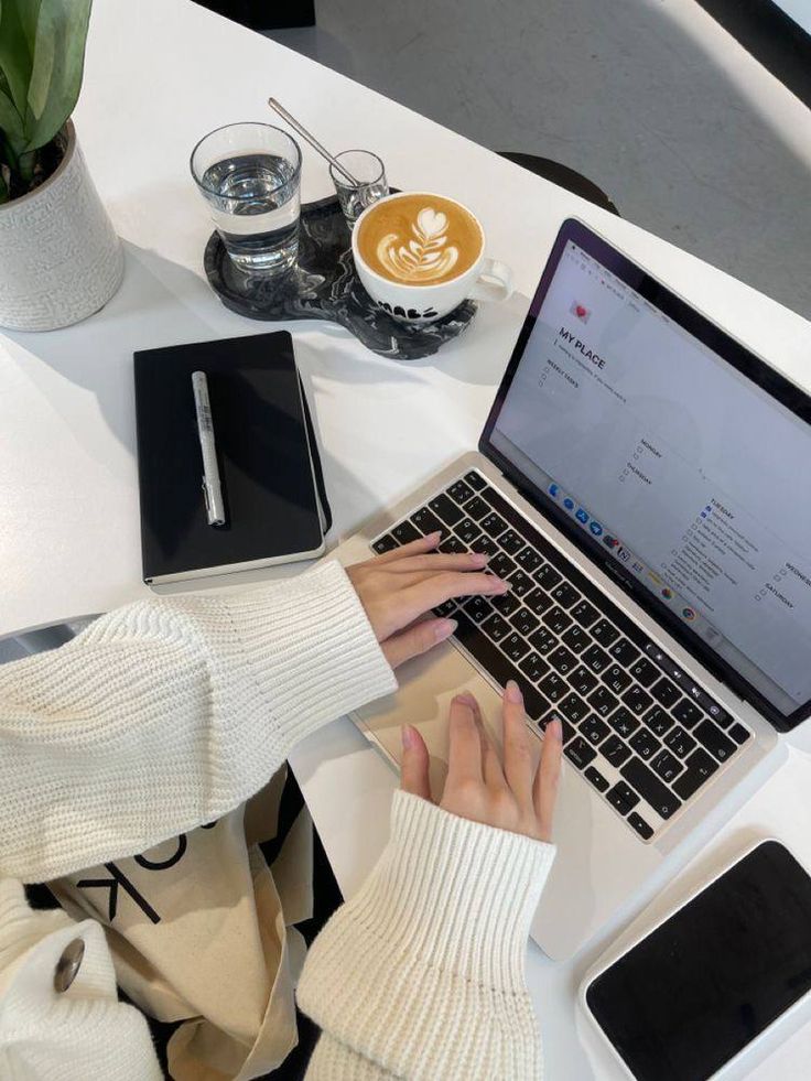 This may contain: a woman sitting at a table with her laptop and cell phone in front of her