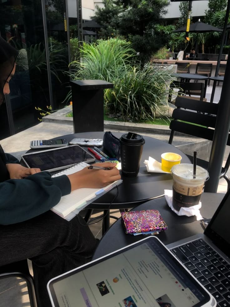This may contain: a woman sitting at a table with two laptops and a tablet on her lap
