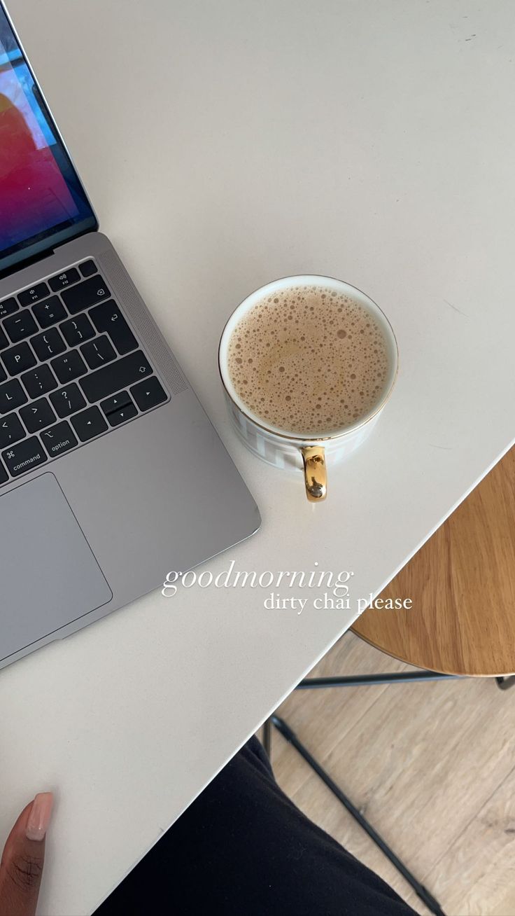 This may contain: an open laptop computer sitting on top of a table next to a cup of coffee