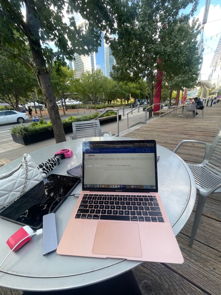 This may contain: an open laptop computer sitting on top of a table next to a white chair and tree