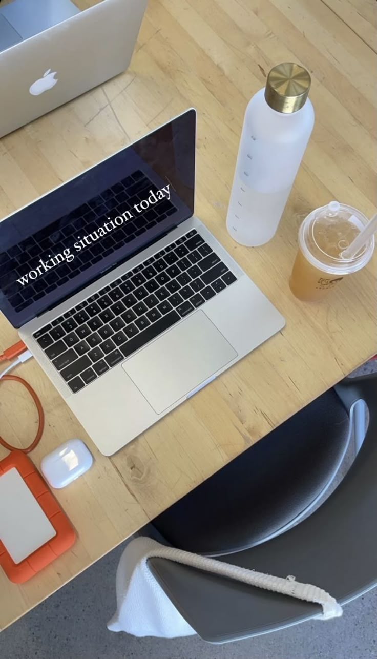 This may contain: an open laptop computer sitting on top of a wooden desk next to a cup and other items
