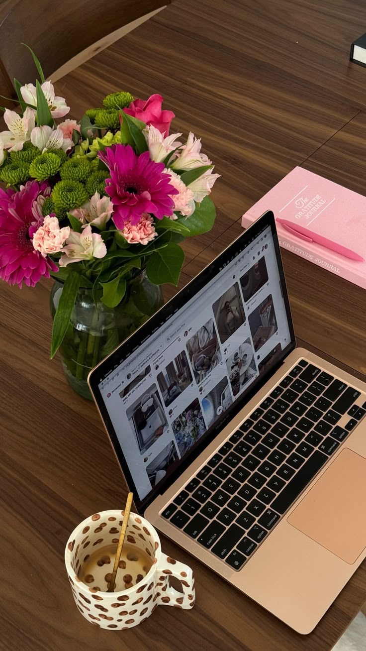 This may contain: an open laptop computer sitting on top of a wooden desk next to a vase with flowers
