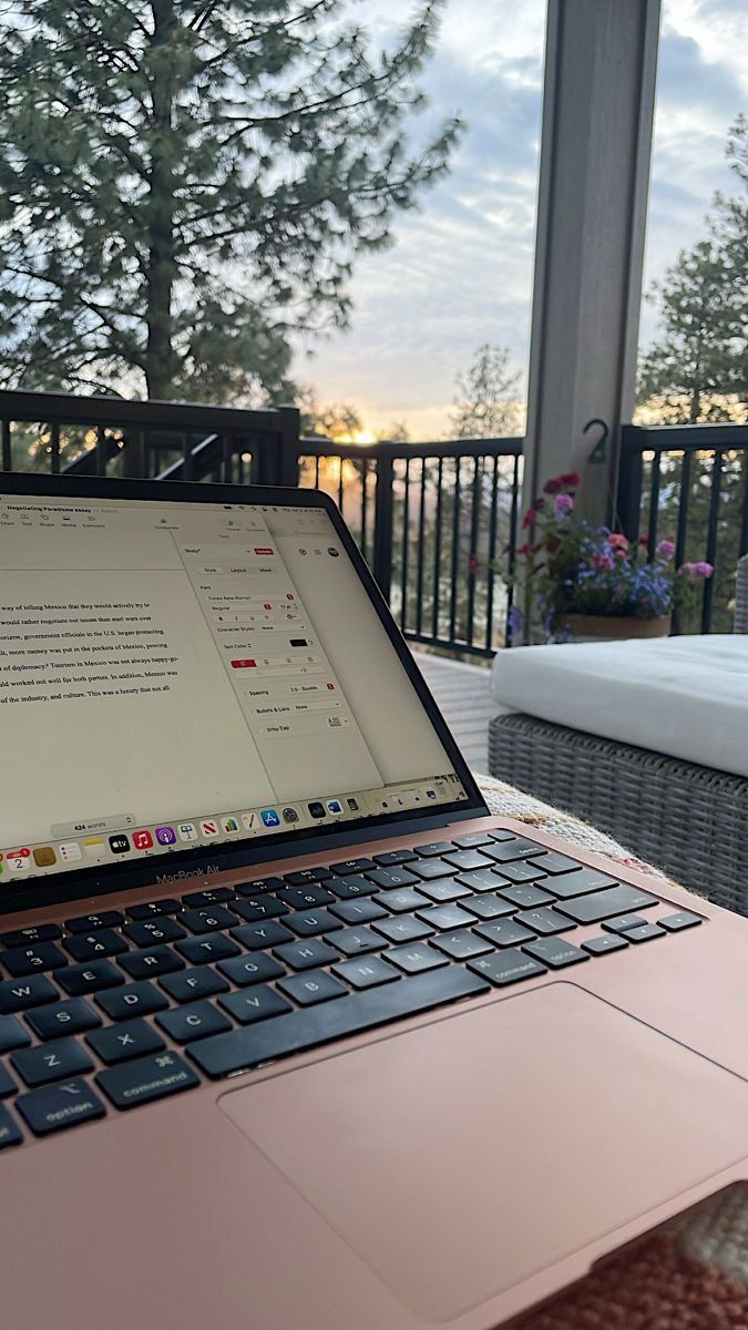 This may contain: an open laptop computer sitting on top of a wooden table next to a bed and balcony