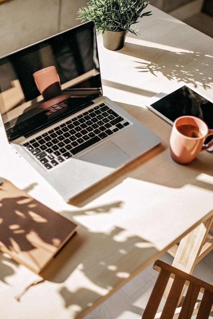 This may contain: an open laptop computer sitting on top of a wooden table next to a cup of coffee
