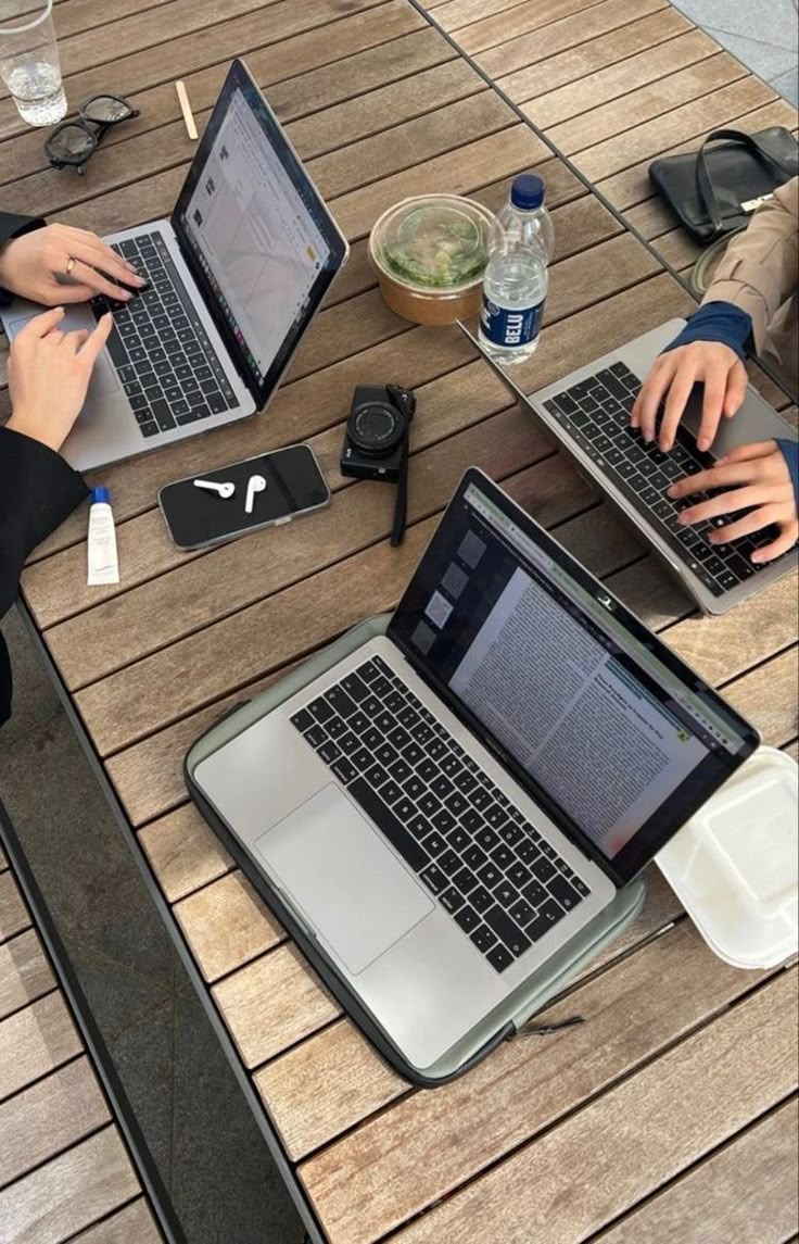 This may contain: three people sitting at a table with laptops on their lap tops, one is typing