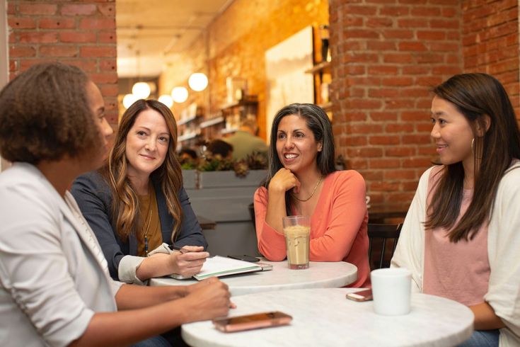 This may contain: three women sitting at a table talking to each other and drinking coffee in a restaurant