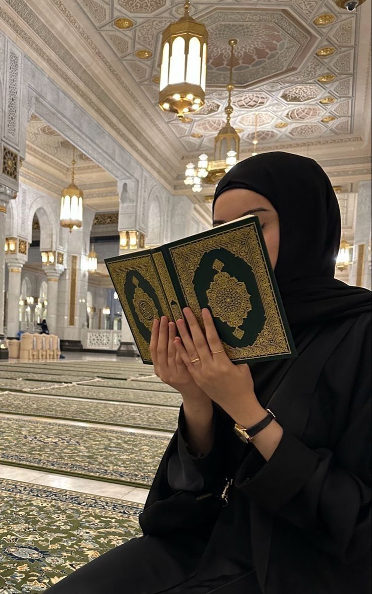 This may contain: a woman wearing a black hijab is holding a book in front of her face